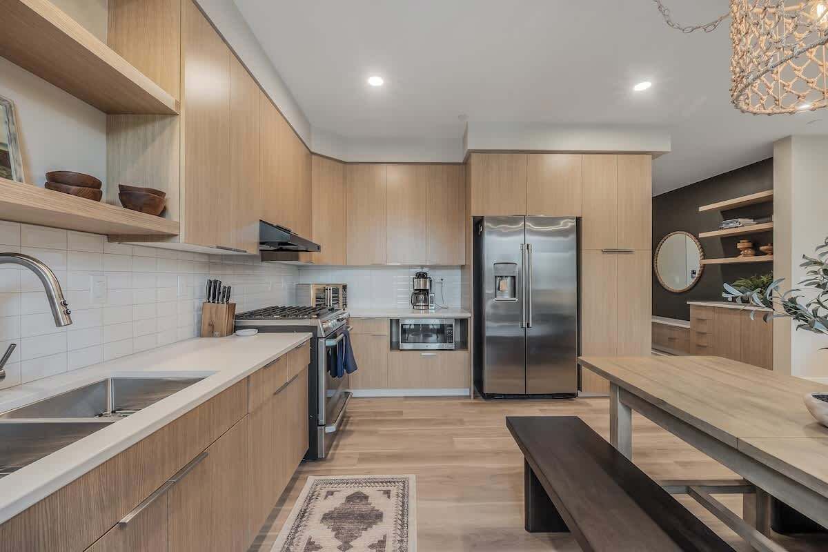 Eine moderne Küche mit Holzschränken, einem Edelstahlkühlschrank, einem eingebauten Ofen und einer Kaffeemaschine.