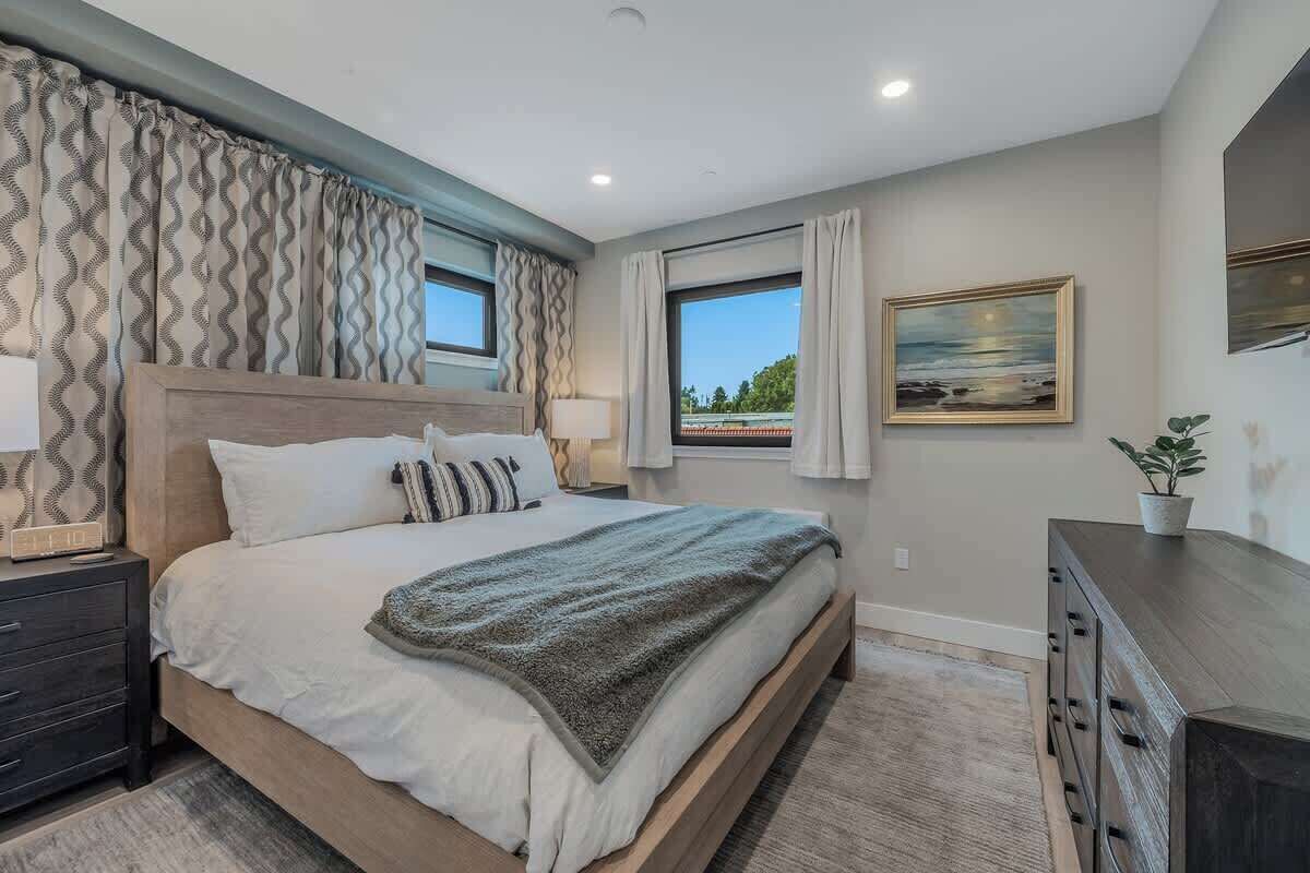 A bedroom with a large bed, a nightstand, a dresser, and a window with curtains.