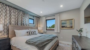Un dormitorio con una cama grande, una mesita de noche, un aparador y una ventana con cortinas.
