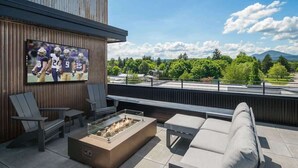 Un área de estar exterior moderna con televisión de pantalla plana, asientos cómodos y un brasero.