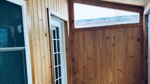 Une pièce aux murs en bois, avec une grande fenêtre, une porte et un paillasson noir à l’entrée.