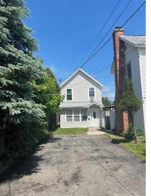 A two-story house with a front porch, a chimney, and a driveway leading to the entrance.