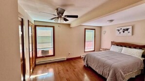 Une chambre à coucher avec un lit, un ventilateur de plafond et deux fenêtres équipées de stores.