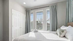 A bedroom with a large bed, a window with blinds, and a door.