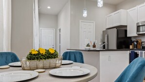 A modern kitchen with white cabinets, a stainless steel refrigerator, and a dining area with a round table and blue chairs.