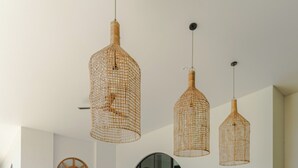 A dining area with a wooden table and wicker chairs, three woven pendant lights, and a large mirror above the table. - Villa Sungai (Cepaka)