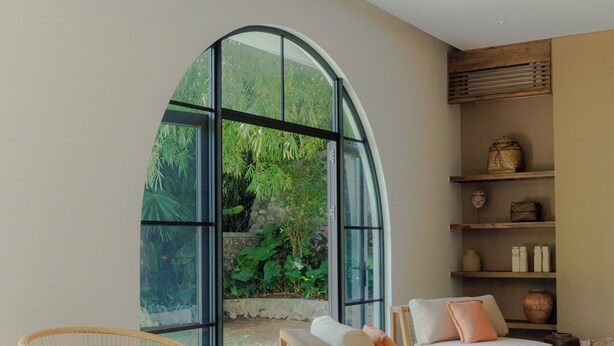 A modern living room with a large arched window, wicker furniture, a wooden coffee table, and a zebra-patterned rug. - Villa Sungai (Cepaka)