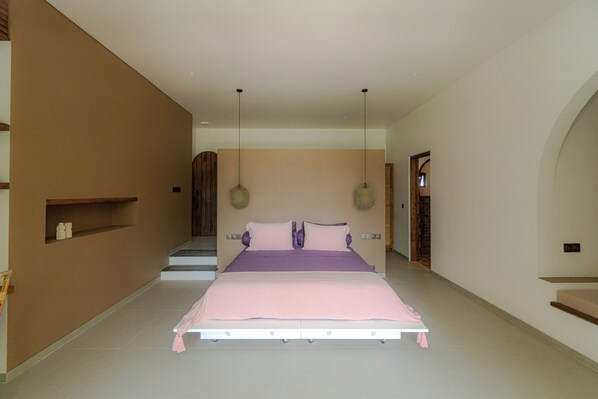 A bedroom with a large bed, a built-in shelf, and a staircase leading to another room. - Villa Sungai (Cepaka)