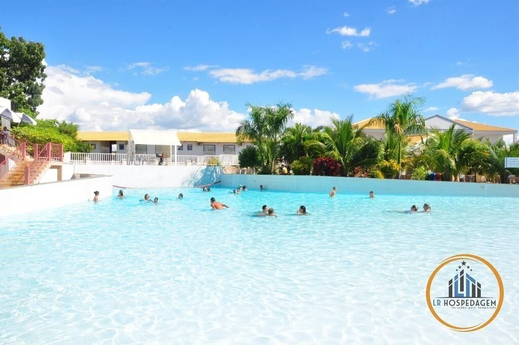 Une piscine où des gens nagent et s’amusent, entourée de bâtiments et de palmiers.