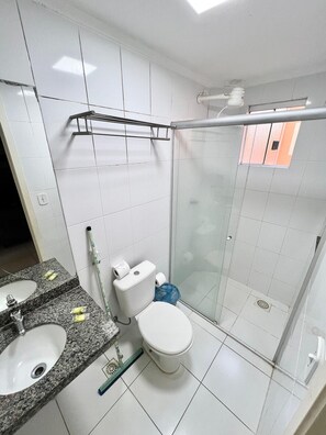 Ein Badezimmer mit Toilette, einem Waschbecken mit Granitplatte und einer Duschkabine aus Glas.