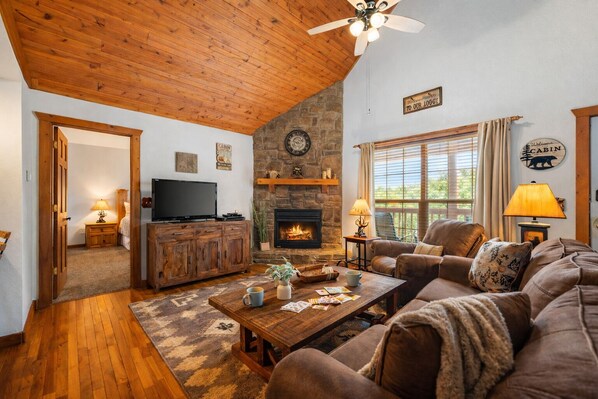 A cozy living room with a stone fireplace, wooden ceiling, and a television on a wooden cabinet. - Stonebridge Resort Getaway Pools, Golf, Family Fun (Branson West)