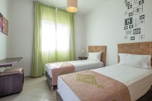 A hotel room with two beds, a desk, a chair, a lamp, and a wall with geometric patterns. - Lunja Village Taghazout (Tamri)