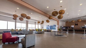 Een ruime lobby met banken, een rode fauteuil, een ronde tafel en hangende rieten lampen.