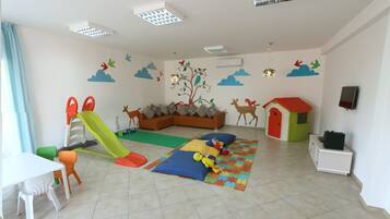 Una sala de juegos con un tobogán, alfombras de juego y un sofá.