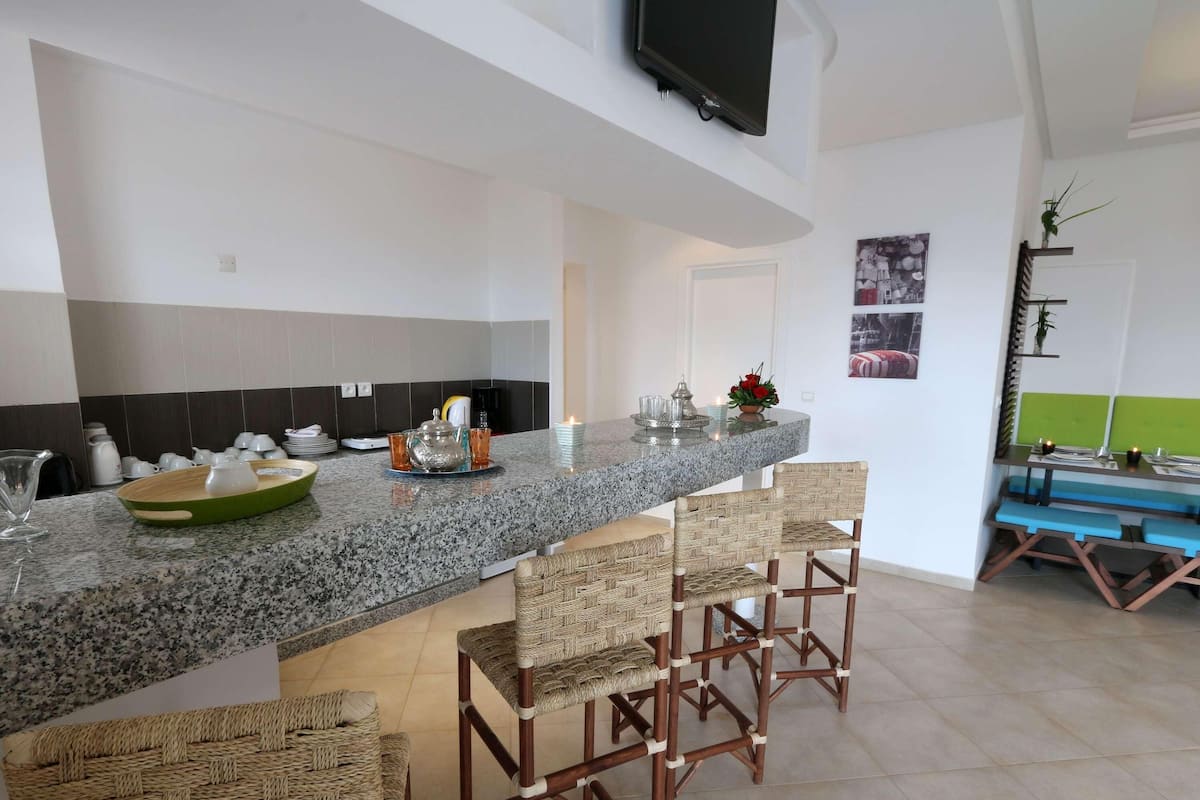 Una cocina con encimera de granito, taburetes de bar y un televisor montado en la pared.
