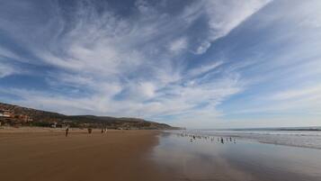Une vaste plage de sable fin, sous un ciel dégagé, avec des collines qui se dessinent à l’horizon.