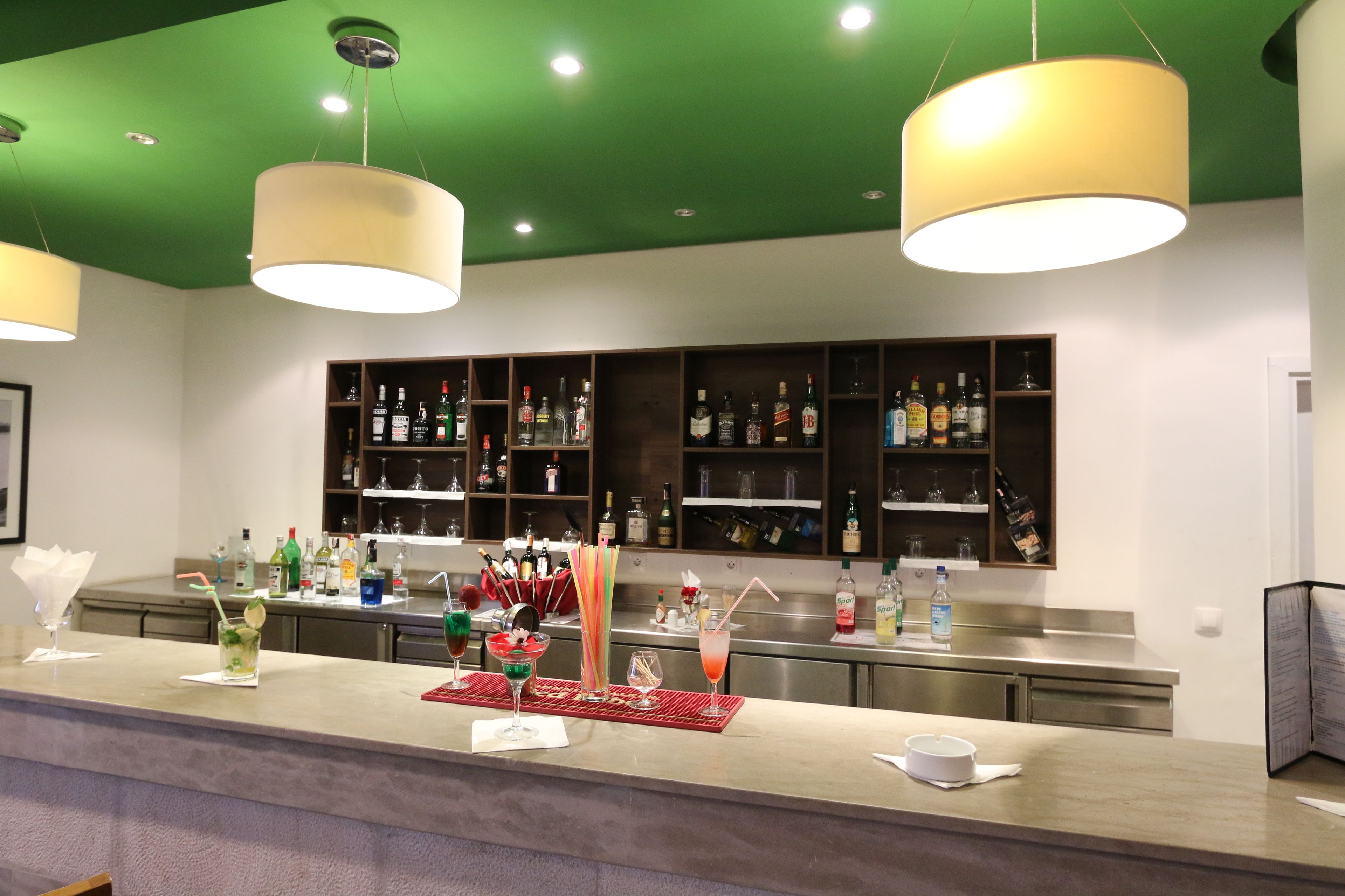 Una zona de bar con techo verde, lámparas colgantes y estantes llenos de botellas de licores.