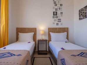 A hotel room with two beds, a nightstand, a lamp, and a wall with decorative patterns. - Lunja Village Taghazout (Tamri)