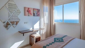 Een slaapkamer met een bed, nachtkastje, spiegel en een raam met uitzicht.