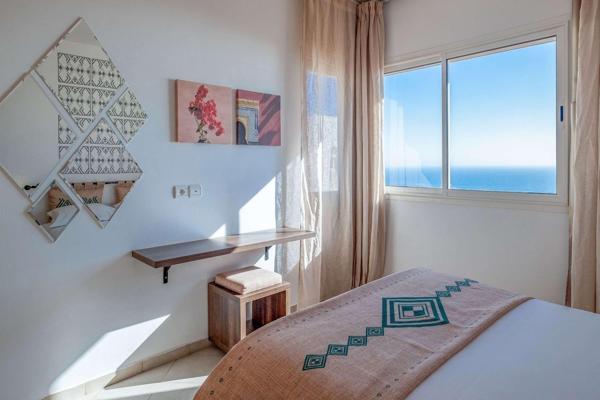 Un dormitorio con una cama, una mesita de noche, un espejo y una ventana con vistas.
