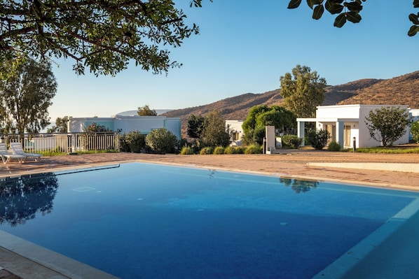 A swimming pool with lounge chairs, surrounded by buildings and hills. - Lunja Village Taghazout (Tamri)