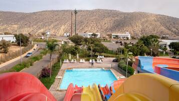 Une piscine avec des toboggans, un espace de stationnement et un paysage montagneux en arrière-plan.