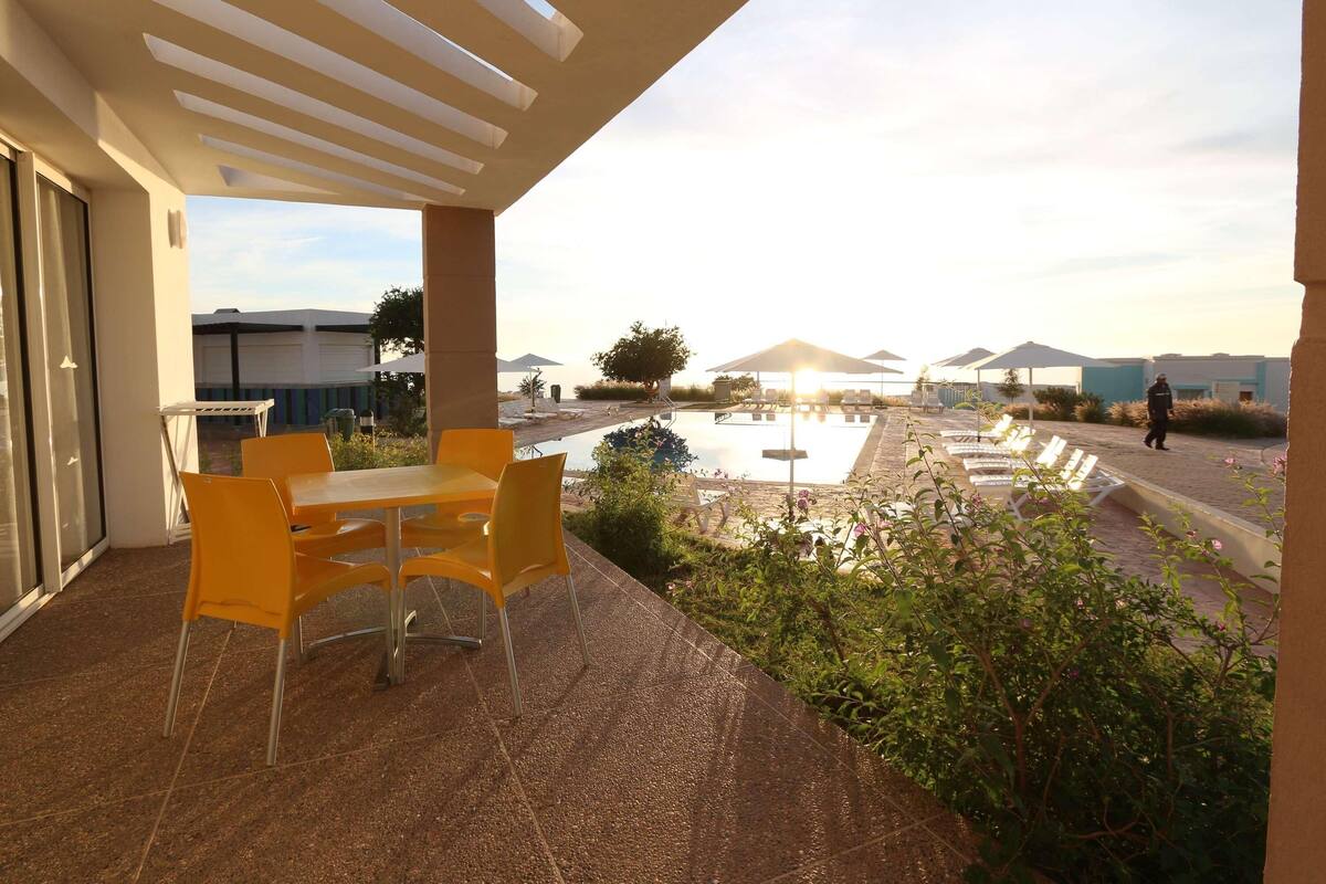 Un espacio exterior cubierto con piscina, sillas amarillas y vistas del paisaje circundante.