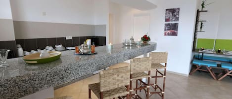 A kitchen with a granite countertop, bar stools, and a television mounted on the wall.