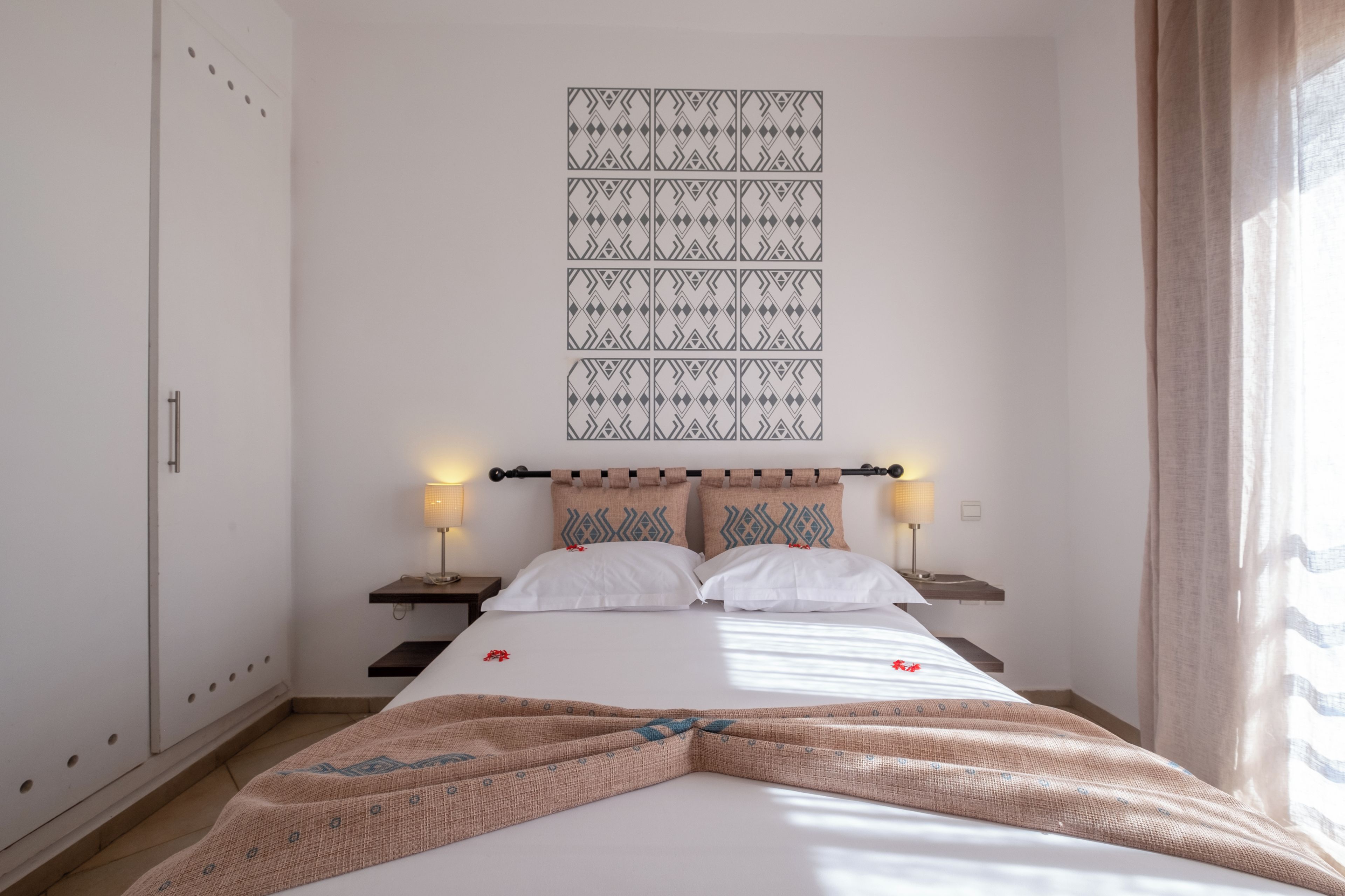 Une chambre d’hôtel comprenant un lit, deux tables de chevet, un luminaire fixé au mur et une tapisserie à motifs.