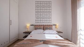 Une chambre d’hôtel comprenant un lit, deux tables de chevet, un luminaire fixé au mur et une tapisserie à motifs.