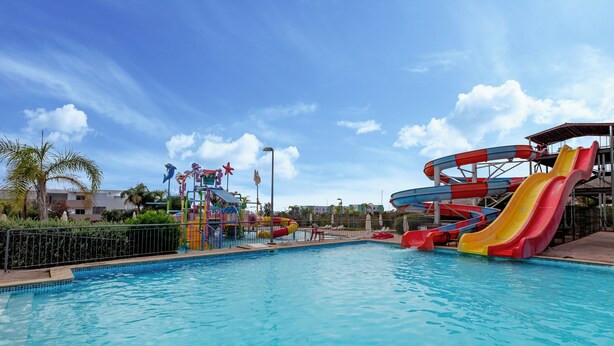 A swimming pool with water slides and a palm tree. - Lunja Village Taghazout (Tamri)