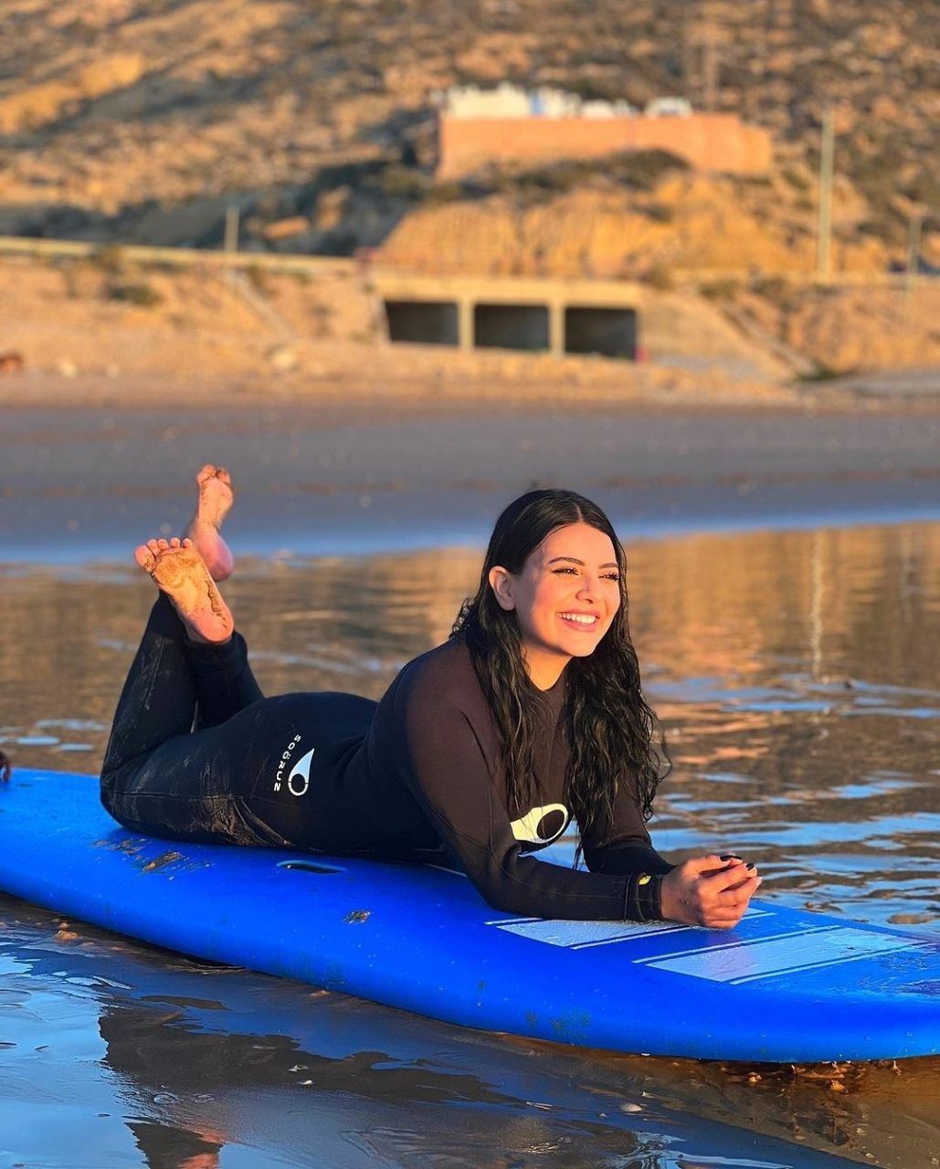Eine Person liegt auf einem blauen Surfbrett im seichten Wasser.