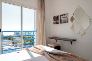 A hotel room with a large window, a bed with a blanket, a small stool, and a shelf with pictures. - Lunja Village Taghazout (Tamri)
