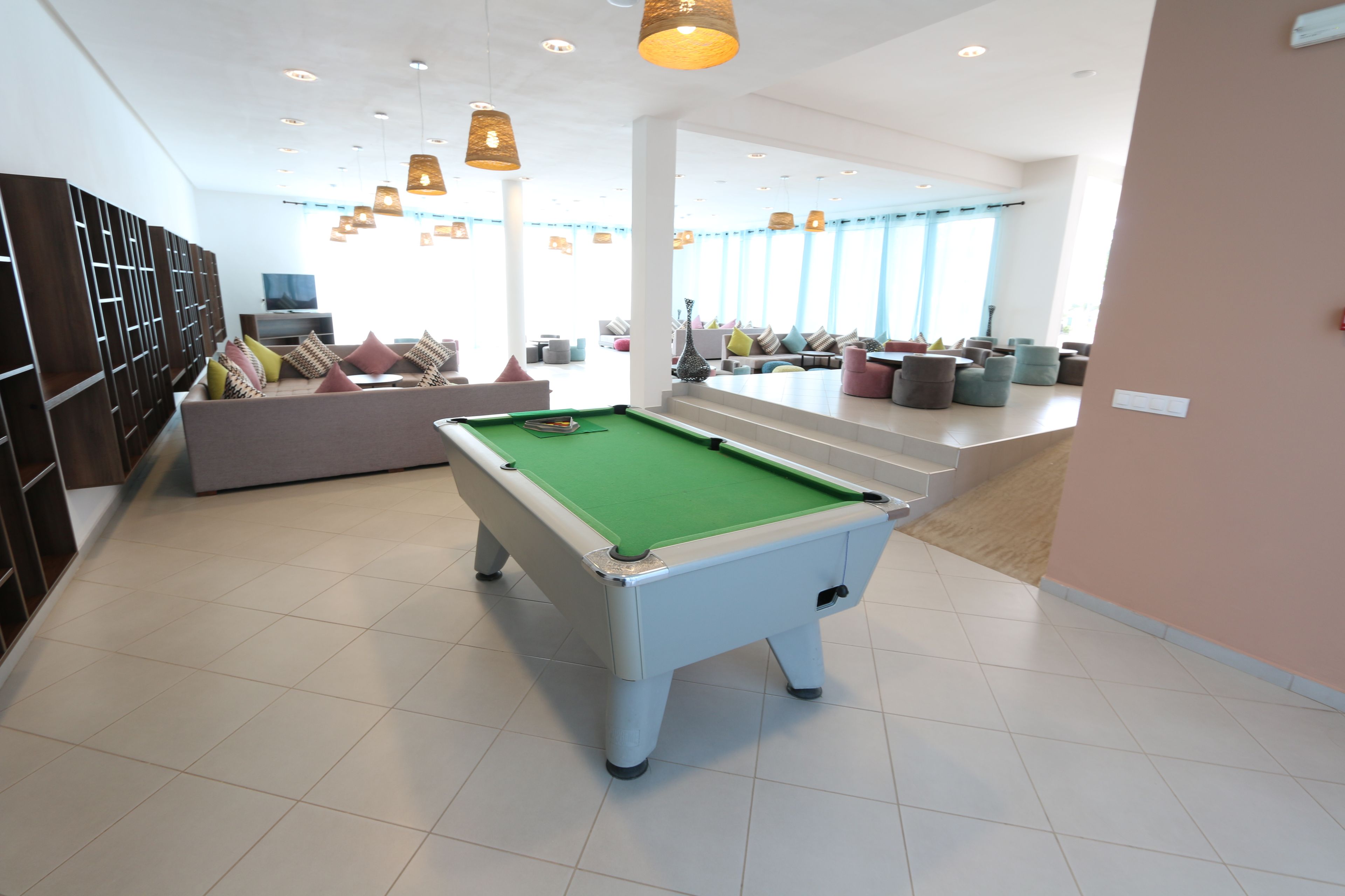 Ein Billardtisch in einem modernen Raum mit einer Couch, Stühlen, einem Fernseher und einer Treppe zu einem weiteren Bereich.