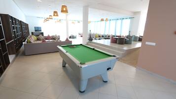 Ein Billardtisch in einem modernen Raum mit einer Couch, Stühlen, einem Fernseher und einer Treppe zu einem weiteren Bereich.
