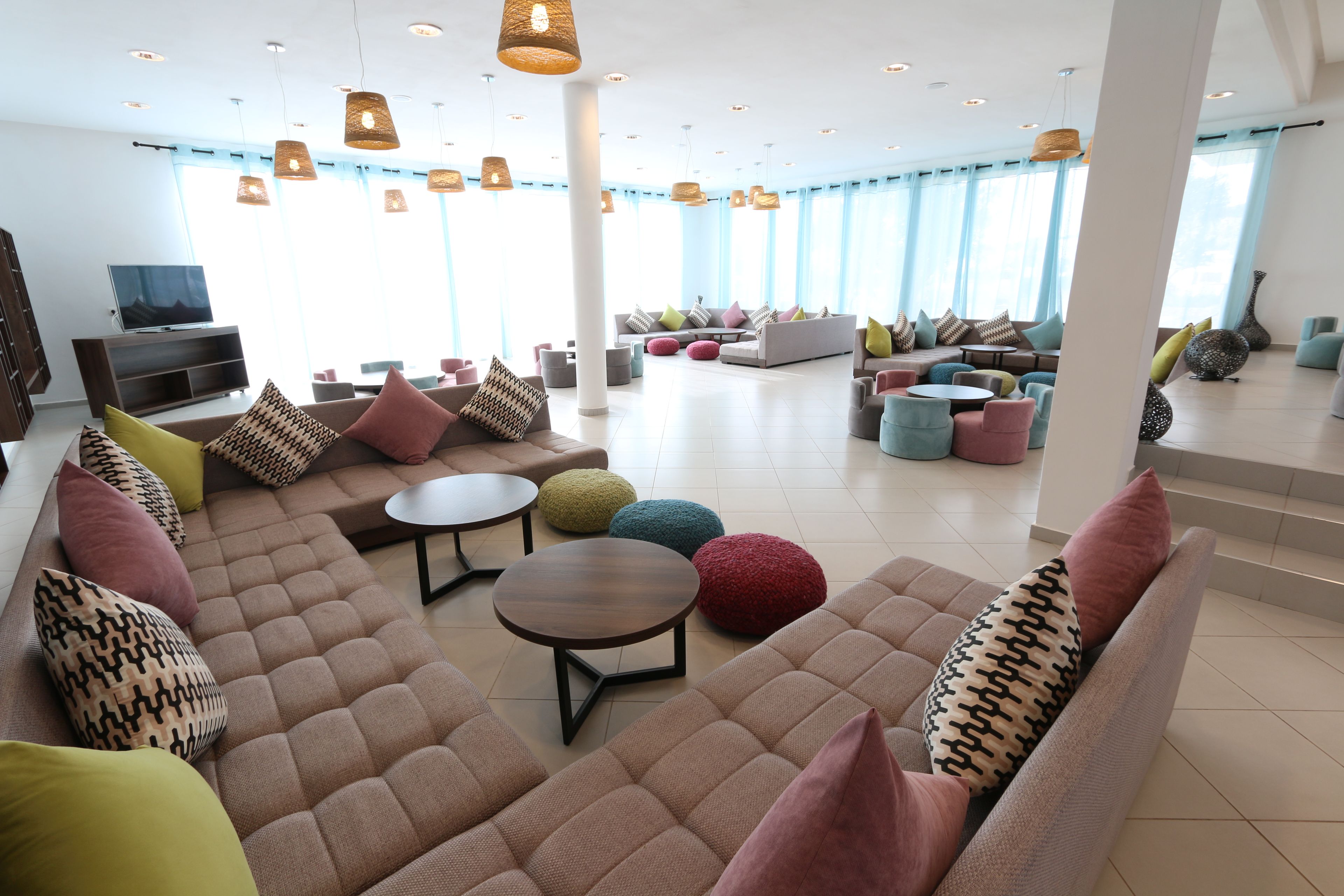 A spacious lounge area with multiple seating options, including sofas and round tables, and a television on the left.