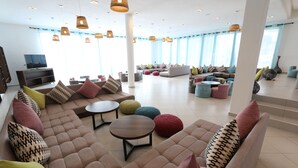 A spacious lounge area with multiple seating options, including sofas and round tables, and a television on the left. - Lunja Village Taghazout (Tamri)