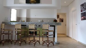 A modern kitchen with a TV, bar stools, and a granite countertop. - Lunja Village Taghazout (Tamri)