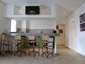 Una cocina moderna con televisión, taburetes de bar y encimera de granito.