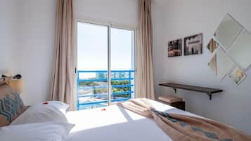 Une chambre d’hôtel avec un lit, une banquette, un bureau, une grande fenêtre avec des rideaux et une vue sur un balcon bleu.