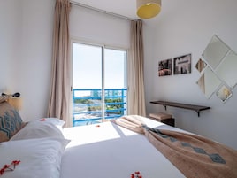 Una habitación de hotel con cama, un banco, un escritorio, un ventanal con cortinas y vistas a un balcón azul.