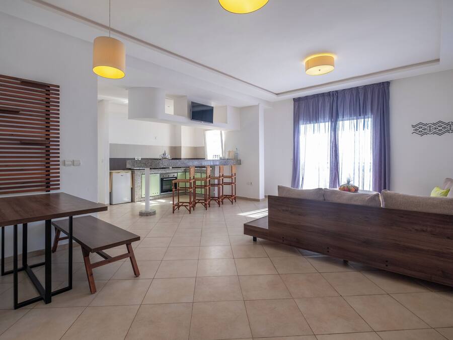 A modern living room with a sofa, a dining table, and a kitchen in the background.