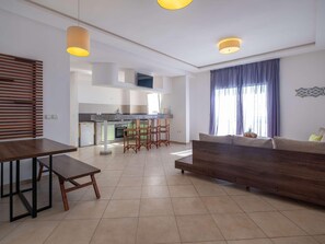 A modern living room with a sofa, a dining table, and a kitchen in the background. - Lunja Village Taghazout (Tamri)