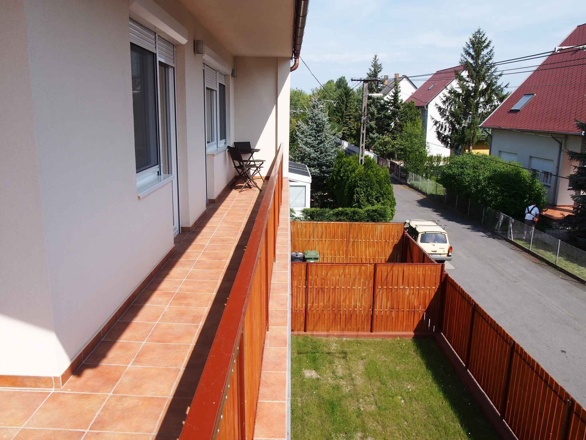 A balcony with a tiled floor, a wooden fence, and a view of a street with houses and a parked car.