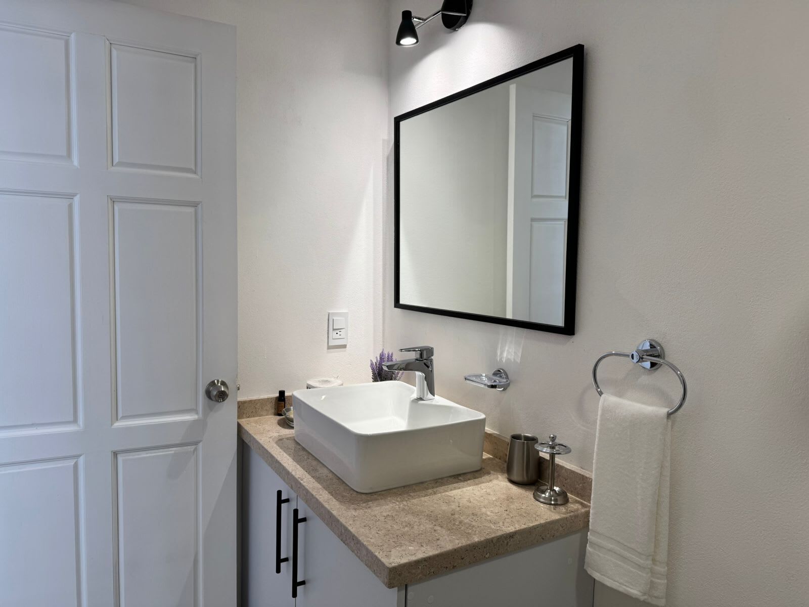 A modern bathroom with a white sink, a large mirror, and a towel rack.