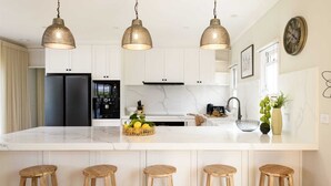 A modern kitchen with white cabinets, a marble countertop, and three hanging pendant lights. - Ashbourne Farmhouse Near Woodend (Ashbourne)