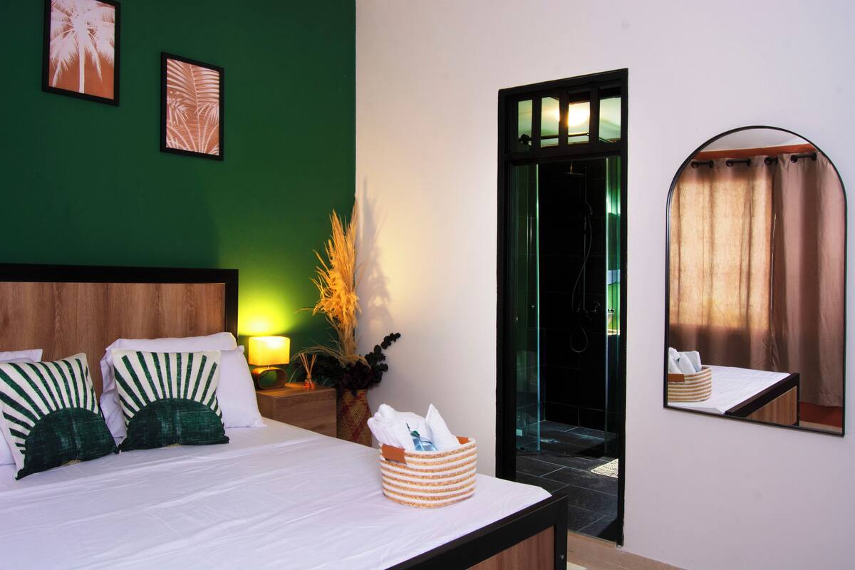 A hotel room with a bed, a bedside table with a basket, a mirror, and framed pictures on the wall.