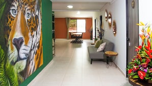 A hallway with a large painting of a leopard's face, a sofa with cushions, a small round table, and a potted plant with colorful flowers. - Bohemia Boutique Hostel (Cali)
