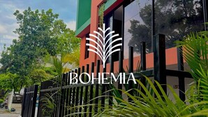 A modern building with a green and red facade, a black metal fence, and lush greenery. - Bohemia Boutique Hostel (Cali)