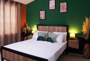A neatly made bed with white linens and green decorative pillows, a wooden headboard, and a green wall with framed artwork. - Bohemia Boutique Hostel (Cali)